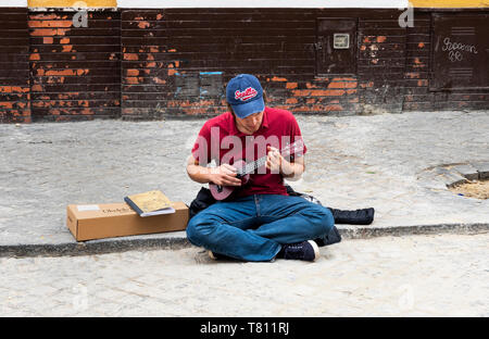 Young man busking on a street in Seville playing a ukulele Stock Photo