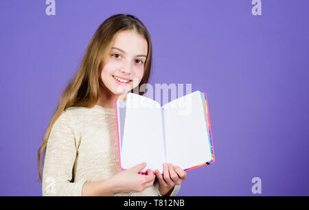 Book concept. Childhood literature. Development and education. Reading skill. Personal diary. Notepad planner. School stationery. Learn more. Girl hold book violet background. Kid show book notepad. Stock Photo