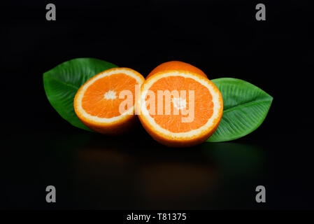 two half ripe orange fruit useful with leaf on an isolated black background Stock Photo