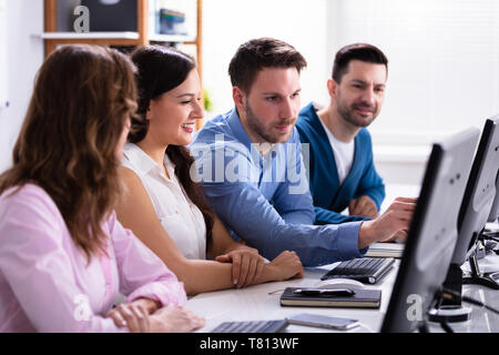 Businessman Pointing On Computer Screen While Talking With Her Colleague Stock Photo