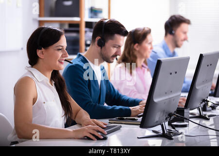 Happy Young Customer Service Executives Using Earphones Working In Call Center Stock Photo