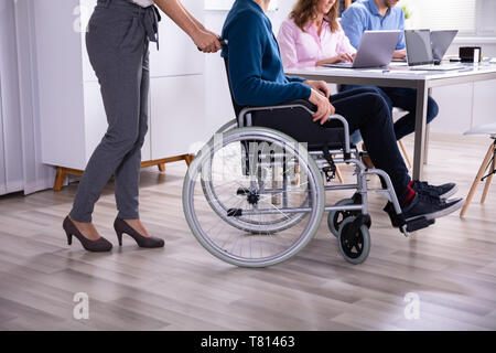 Smiling Young Businesswoman Helping Disabled Colleague In Wheelchair Stock Photo