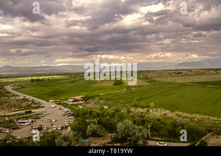 Ararat valley with darkened spring sky above the road leading to the medieval monastery of Khor Virap among gardens and vineyards on the background of Stock Photo