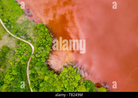 Aerial view of colorful red copper mining waste water in contrast with fresh green forest by drone Stock Photo