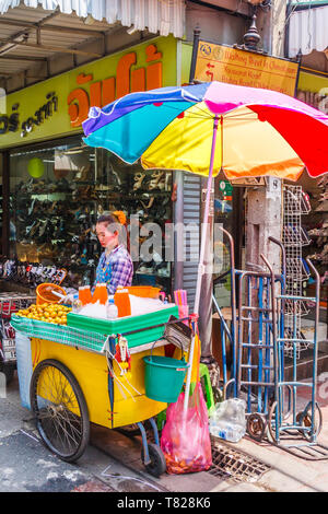 Bangkok, Thailand - April 21st 2011. Orange juice vendor under a colourful umbrella. Fruit juices are a popular drinl. Stock Photo