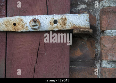 A fragment of an old wooden door with a rusty hinge. Ein Fragment einer alten Holztür mit einem rostigen Scharnier. Fragment starych drzwi z zawiasą. Stock Photo
