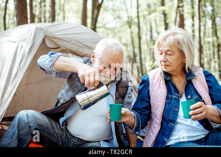 Senior couple pouring coffee having a picnic at the campsite in the forest Stock Photo