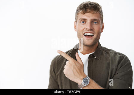 Hey check out this you gonna like it. Portrait of handsome charismatic blond guy with blue eyes and white broad smile pointing at upper left corner Stock Photo