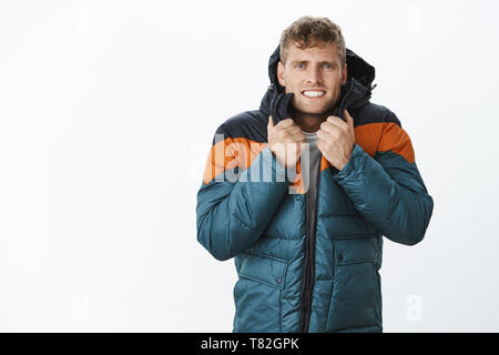 Jeez freezing cold. Portrait of intense trembling handsome european blond man clenching teeth wearing winter puffer jacket suffering from low Stock Photo