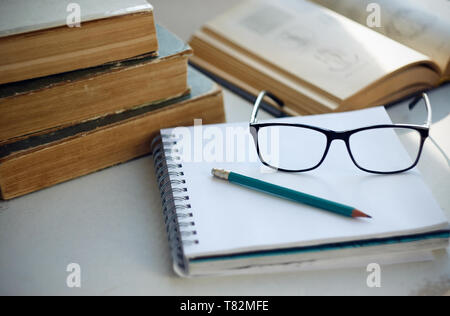 On the table lay an old battered encyclopedias an open notebook on the spring for notes, pencil, glasses and open book with diagrams. Here is a workpl Stock Photo