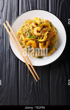 Singapore Noodles Mei Fun with shrimps, sausage, omelet and vegetables close-up on a plate on the table. Vertical top view from above Stock Photo