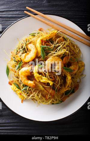 Spicy fried rice noodles with sausage, shrimps and vegetables close-up on a plate on the table. Vertical top view from above Stock Photo