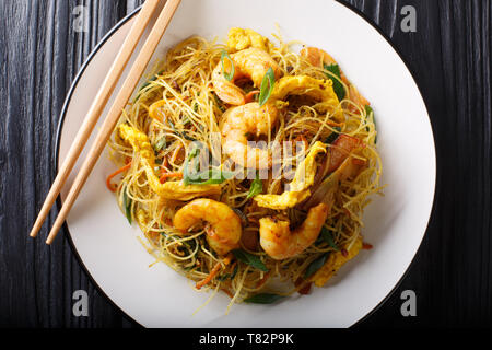 Spicy fried rice noodles with sausage, shrimps and vegetables close-up on a plate on the table. Horizontal top view from above Stock Photo