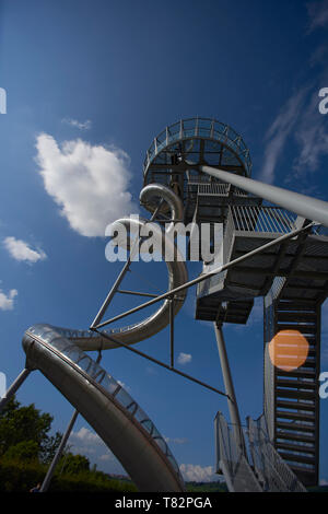 Kids enjoying the beautiful big metal slide at a playground in a park next to the Vitra Design Museum in Weil am Rhein in summer sunshine Stock Photo