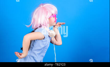 Inspired by music. Little kid listening music. Cute kid with headphones blue background. Small girl headphones pink wig dancing. Child using technology for fun. Modern headphones. Energy motion dance. Stock Photo