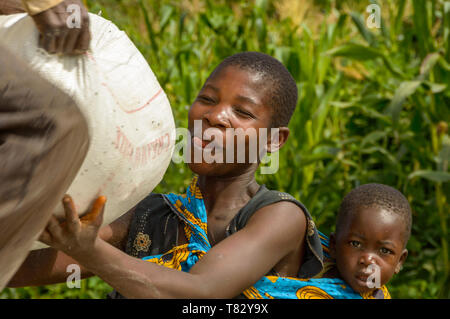 woman with baby on her back collecting bag of maize as relief Stock Photo