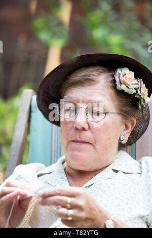 Close up of 1940s woman, 1940 woman, crocheting in garden deck chair, Black Country Museum 1940's WWII wartime summer event, UK. Stock Photo