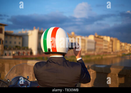 Amazing shot of an Italian man wearing a helmet with the Italian flag standing next to his scooter taking a photo during sunset in Florence, Italy Stock Photo