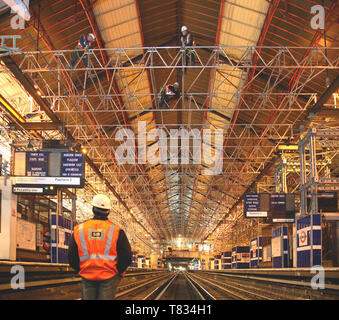 Earls Court station refurbishment, London, UK. A scaffolder watches colleagues installing beams over the tracks during a night-time possession. Stock Photo