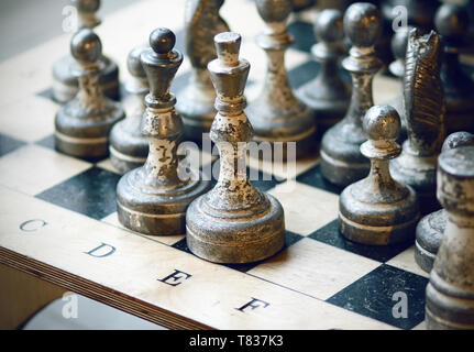 Old chess pieces, with worn silver and black paint, stand on the chessboard in positions Stock Photo