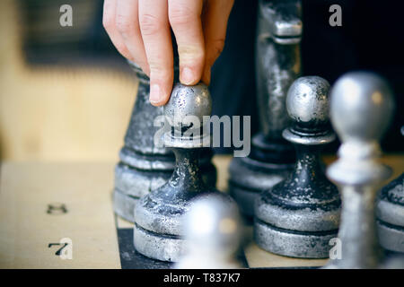 On the Board there are old large shabby chess pieces and the player makes a difficult decision Stock Photo