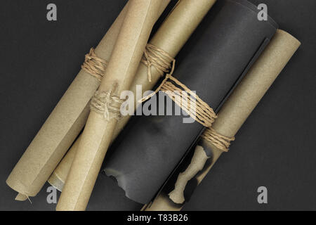Top view of bunch of various twisted and burned beige and black craft scroll papers tied up with beige rope on black matt background Stock Photo