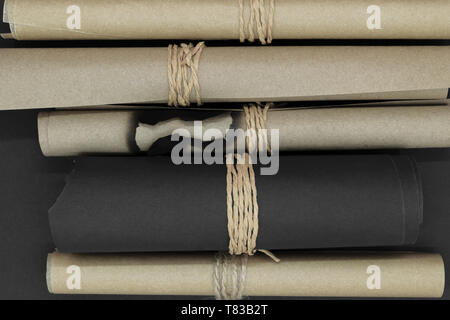 Top view of bunch of various twisted and burned beige and black craft scroll papers tied up with beige rope on black matt background Stock Photo