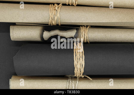Top view of bunch of various twisted and burned beige and black craft scroll papers tied up with beige rope on black matt background Stock Photo