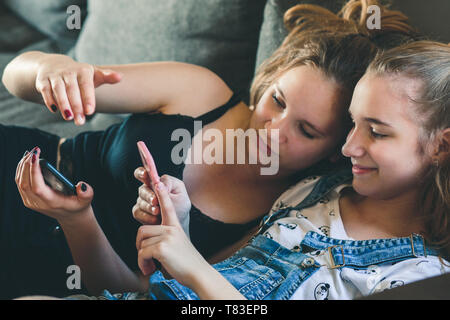 Young women using mobile phones watching music clip, texting, messaging. Teenagers using the smartphones, sitting on sofa at home. Using technology de Stock Photo