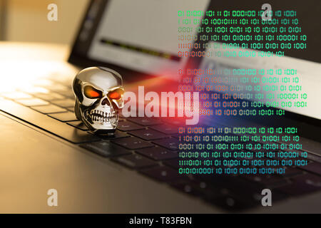 Skull with glowing eyes on a keyboard changes a virtual binary code. Stock Photo