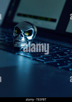 A skull made of shiny metal lies on a keyboard of a computer in dark atmosphere. Stock Photo