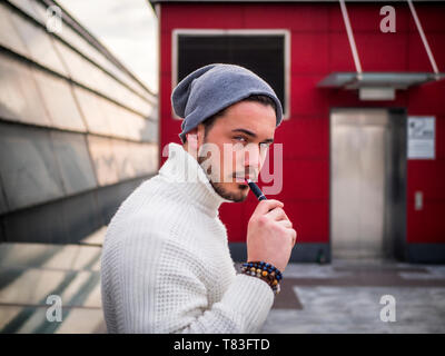 Young man vaping, smoking e-cigarette outdoor Stock Photo