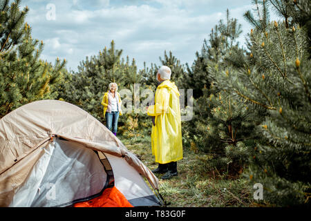 Senior couple in yellow raincoats at the campsite in the young pine forest Stock Photo