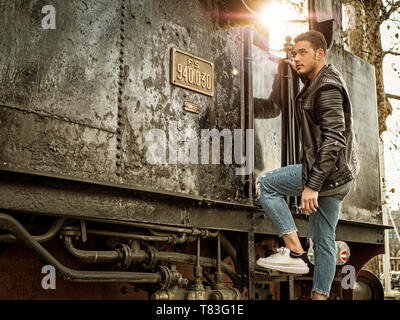 Young man in black leather jacket near old train Stock Photo