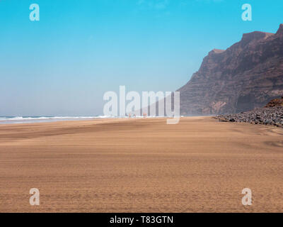 People walking on the Famara seafront, beach and mountains overlooking the ocean. Lanzarote, Canary Islands, Spain. Africa Stock Photo
