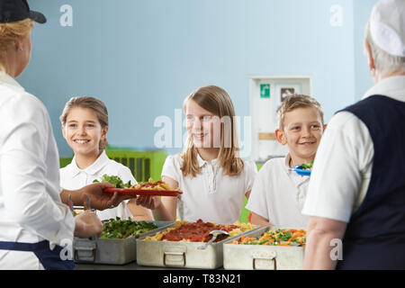 Pupils In School Cafeteria Being Served Lunch By Dinner Ladies Stock Photo