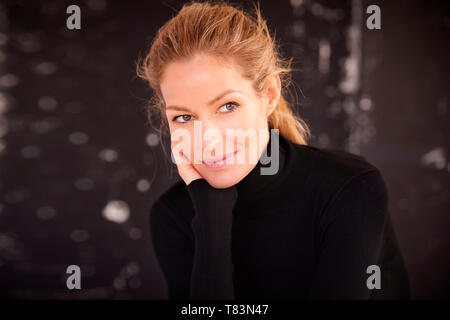 Portrait shot of beautiful blond woman wearing roll neck sweater and deep in thought while sitting at dark background. Stock Photo