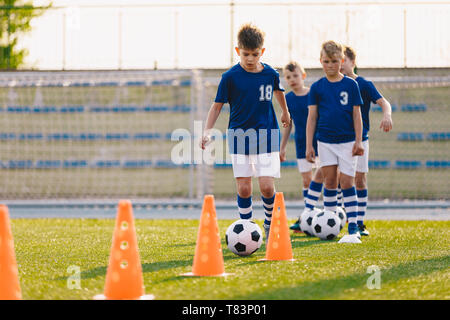 Soccer camp for kids. Boys practice football dribbling in a field. Players develop soccer dribbling skills. Children training with balls and cones Stock Photo