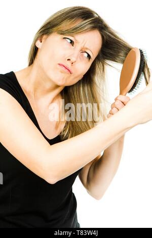 Blond woman having problem with brushing long straight tangled hair with hairbrush - difficult hair dressing - white background Stock Photo