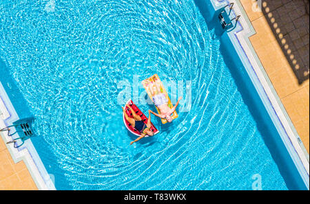 Aerial top vertical view of people old senior couple enjoying the retired lifestyle lay down with trendy coloured lilos inflatable mattress on a blue  Stock Photo