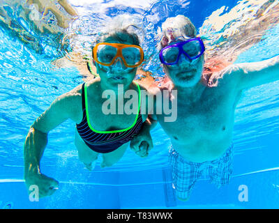 Adult people senior couple have fun swimmin in the pool underwater with coloured funny diving masks - dive concept and active retired man and woman en Stock Photo