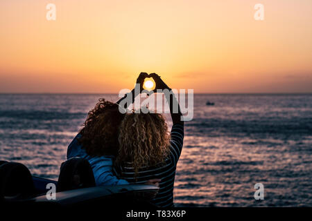 Romantic friendship people concept with two curly lady viewed from back doing hearth love sign with hands to celebrate the summer holiday vacation tra Stock Photo