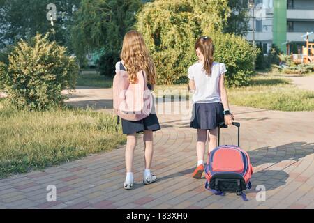 Rear view, two little girls schoolgirls going to school with backpacks, bright sunny day background