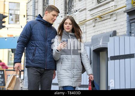 Happy young couple walking and shopping in spring city, beautiful man and woman walking along the street with shopping bags. Stock Photo