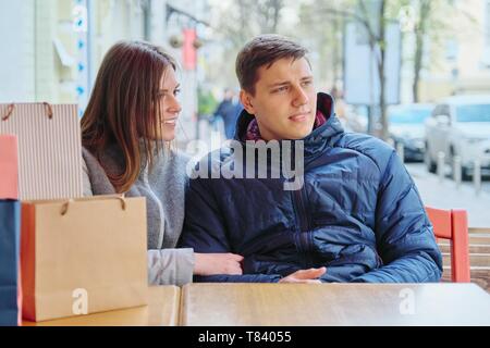 Young talking couple with shopping bags in spring street cafe, waiting for cup of coffee and tea Stock Photo