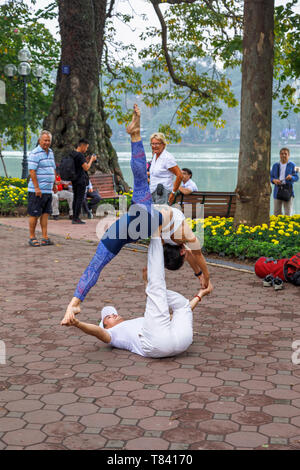 A young couple perform acrobatics on the pavement on the side of Hoan Kiem Lake in the historic centre of Hanoi, north Vietnam, south-east Asia Stock Photo