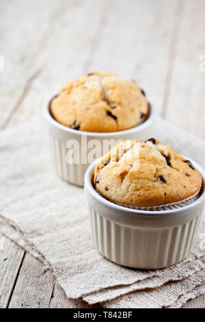 Two homemade fresh muffins on ceramic white bowls on linen napkin on rustic wooden table background. Stock Photo