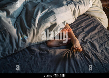 Couple's feet sticking out from under duvet in bed Stock Photo