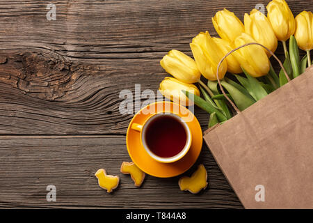 Easter gingerbread cookies, cup of tea on wooden table and yellow tulips. Greeting card. Top view with copy space Stock Photo