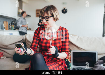 Woman using smartphone at party, friends talking in background Stock Photo
